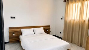 Una camera da letto con un letto con struttura in legno, biancheria bianca, un piccolo comodino e una finestra con tende.