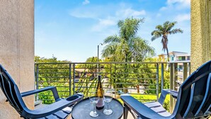 Varanda com mesa, duas cadeiras, uma garrafa de vinho e vista para o verde e edifícios.