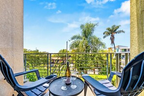 A balcony with a table, two chairs, a bottle of wine, and a view of greenery and buildings. - Heart Of North Park, Mins To Beach & Restaurants (San Diego)