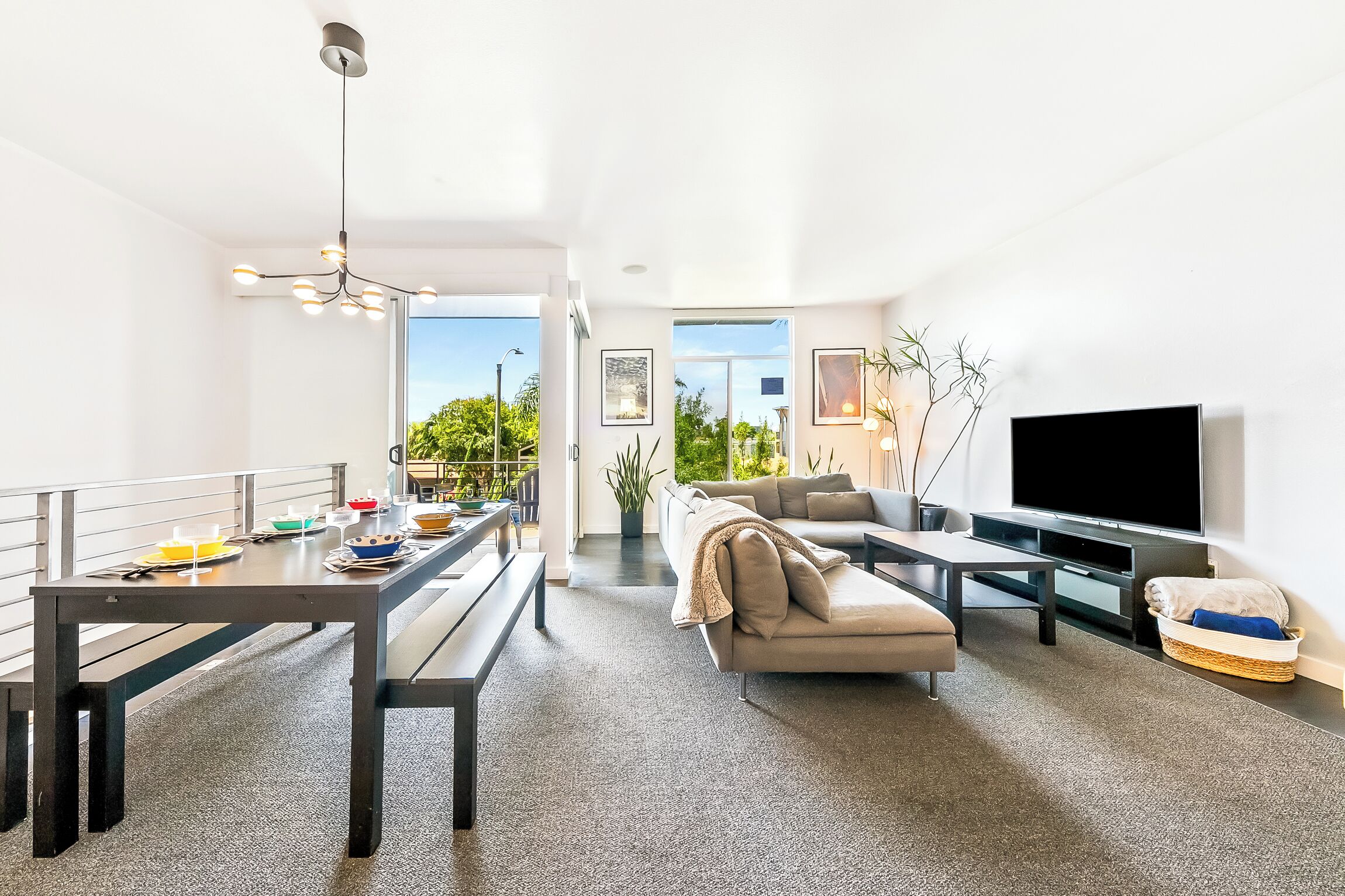 Un salon moderne comprenant un coin repas, un canapé, un téléviseur et un balcon aménagé avec du mobilier d’extérieur.
