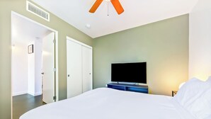 Quarto de hotel com uma cama grande, televisão de tela plana, ventoinha no teto e porta que dá para outro cômodo.