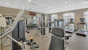 A gym with various exercise equipment, including treadmills and weight machines, and large windows providing natural light. - Fun Family Townhome with Private Pool & Game Room! (Kissimmee)