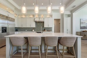 A modern kitchen with a large island, bar stools, pendant lighting, and stainless steel appliances. - Bayfront Retreat 5-min to Vanderbilt Beach (Naples)