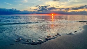Eine Strandansicht mit Fußspuren, die zum Wasser führen, einem Sonnenuntergang und einer ruhigen See.