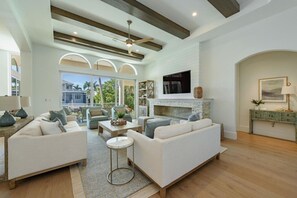 A spacious living room with a fireplace, white sofas, a coffee table, and a TV mounted on the wall. - Bayfront Retreat 5-min to Vanderbilt Beach (Naples)