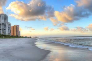 A beach with a sandy shore, a calm sea, and tall buildings in the background. - Bayfront Retreat 5-min to Vanderbilt Beach (Naples)
