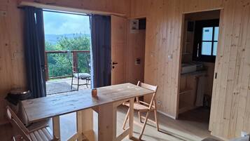 Un intérieur en bois comprenant une table à manger, des chaises, un petit coin cuisine et une vue sur l’extérieur, visible à travers une porte.