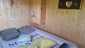 Een kamer met houten lambrisering, een bed, kussens, een lijst met een afbeelding en een klein plankje.