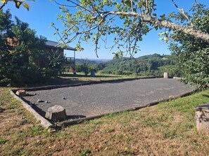 Un espace de stationnement extérieur doté d’une surface pavée, entouré de pelouse et d’arbres, avec un bâtiment visible au loin.