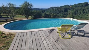 Een zwembad met een houten terras en twee gele stoelen.