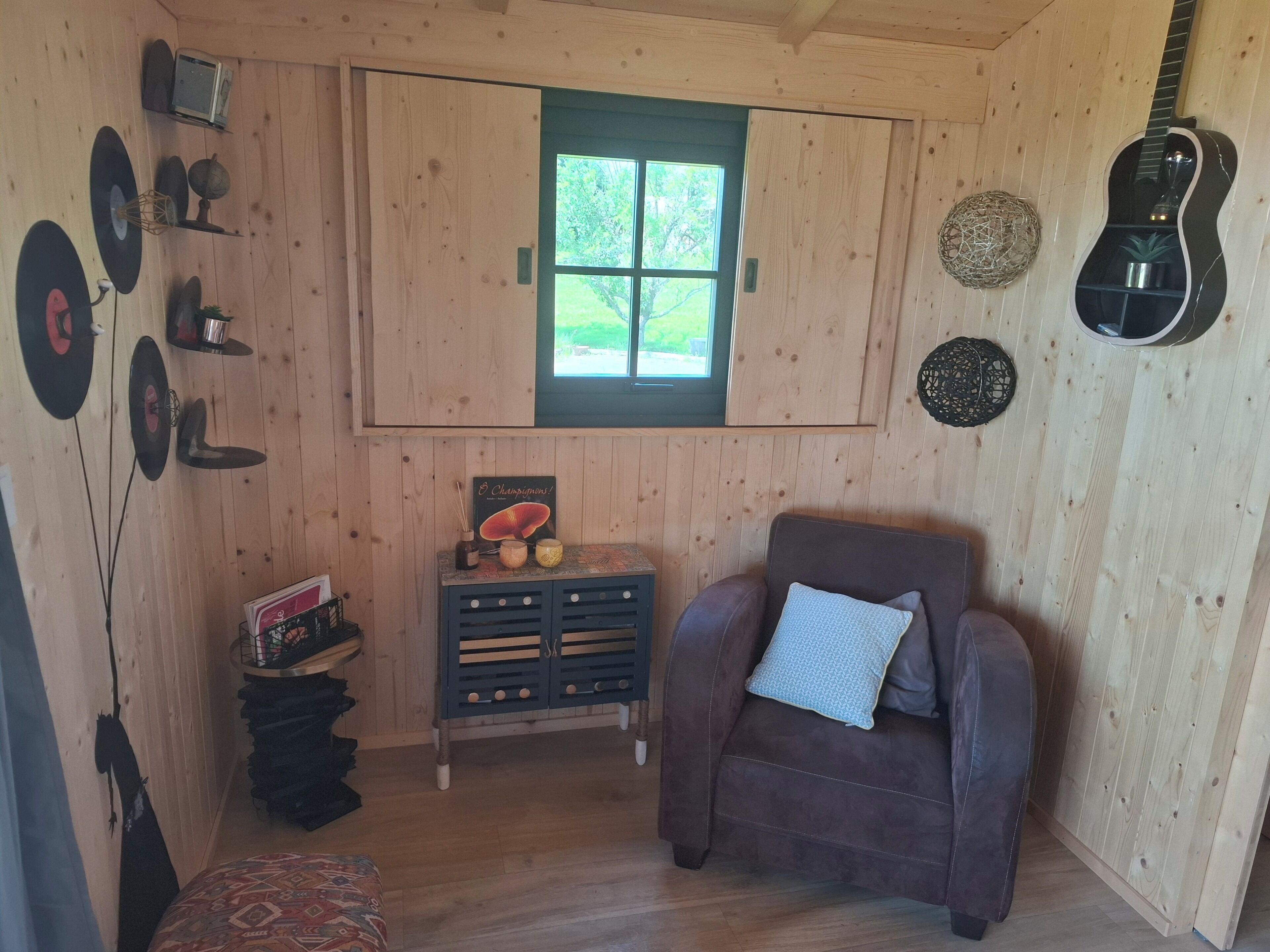 Een houten interieur met een raam, een gitaar, een bank en een bijzettafeltje met decoratieve objecten.