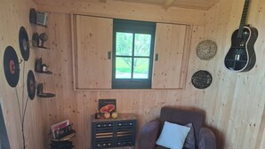 Een houten interieur met een raam, een gitaar, een bank en een bijzettafeltje met decoratieve objecten.