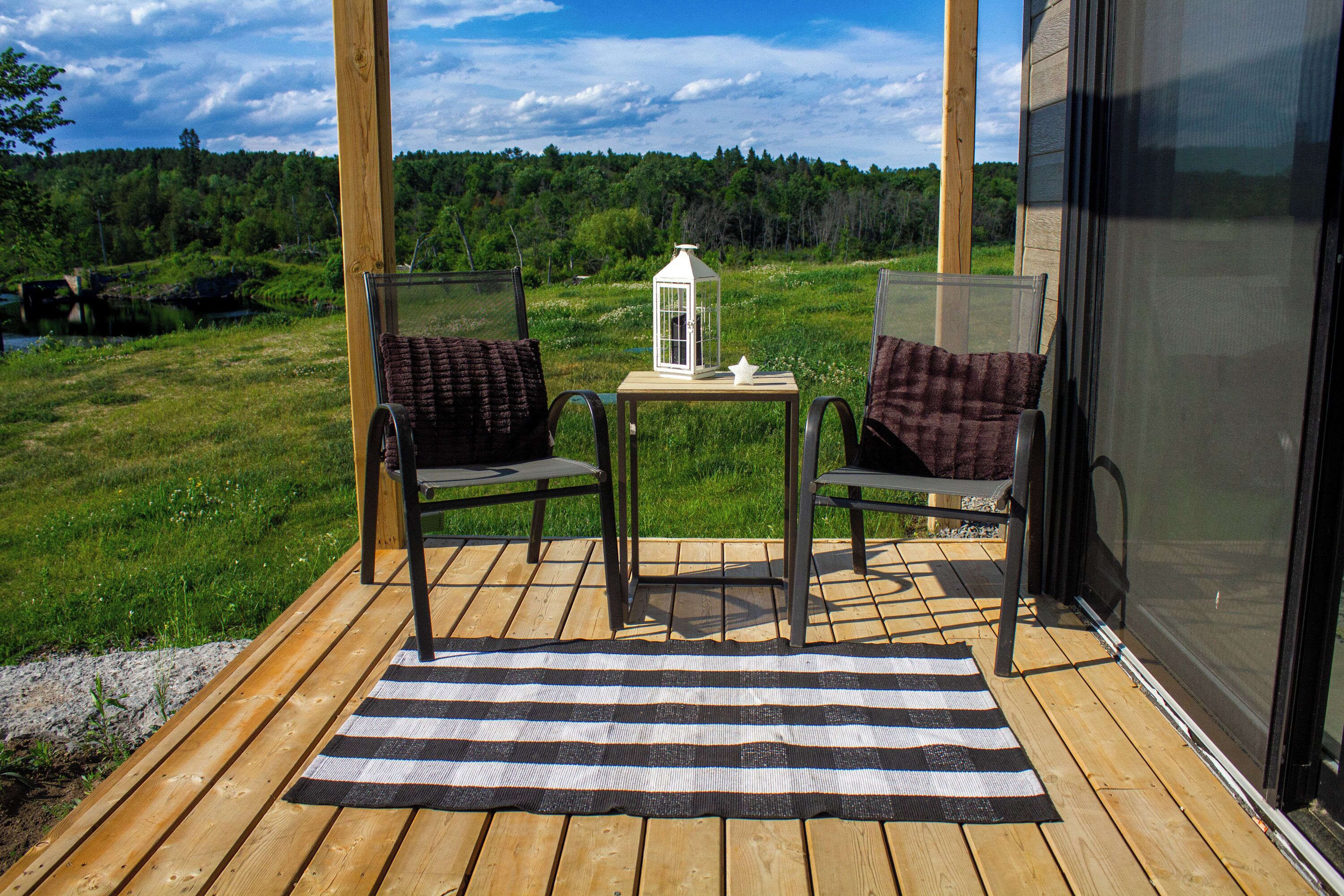 Une terrasse en bois avec deux chaises, une petite table et une lanterne.