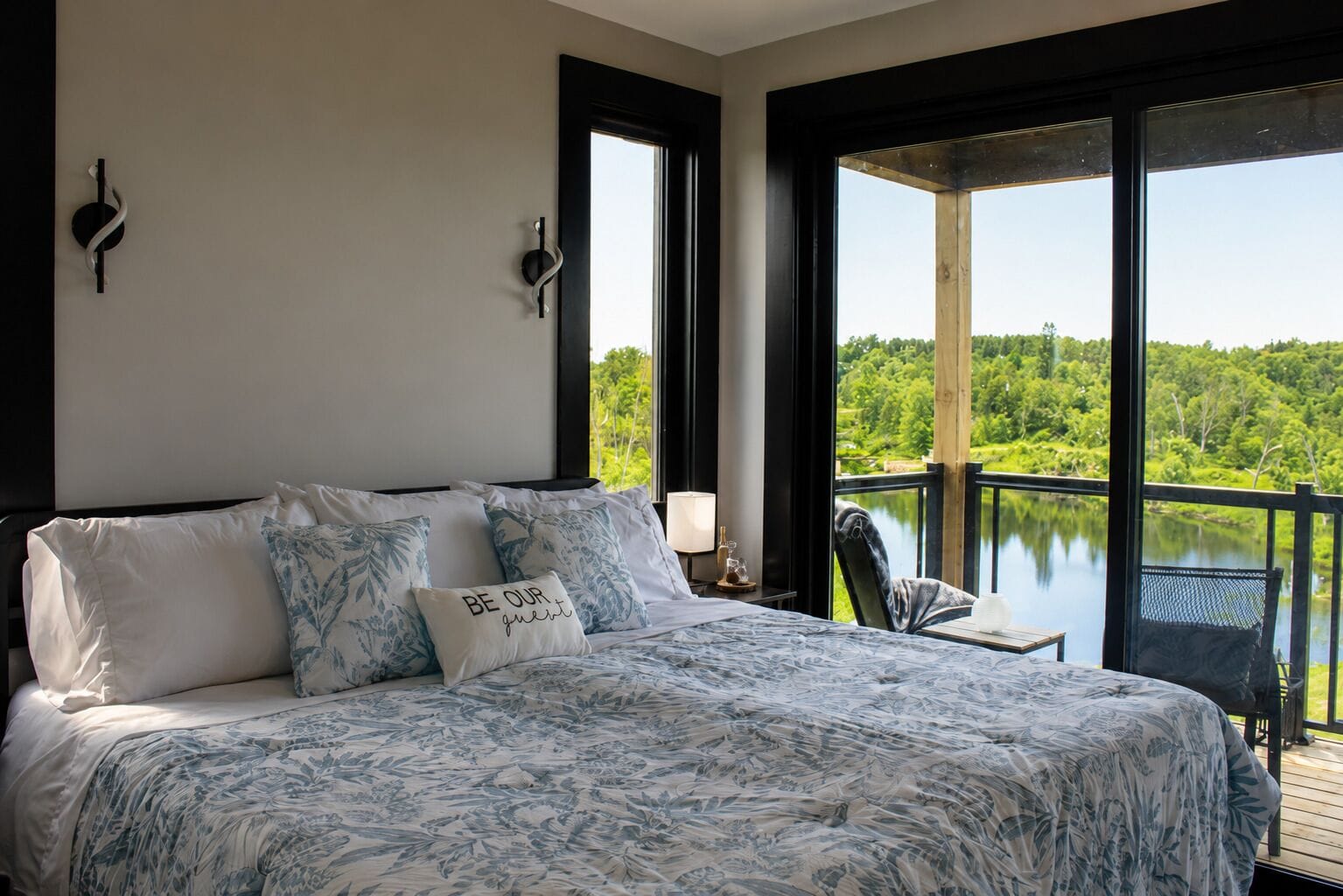Une chambre avec un grand lit, une table de chevet, une lampe et une vue sur un lac.