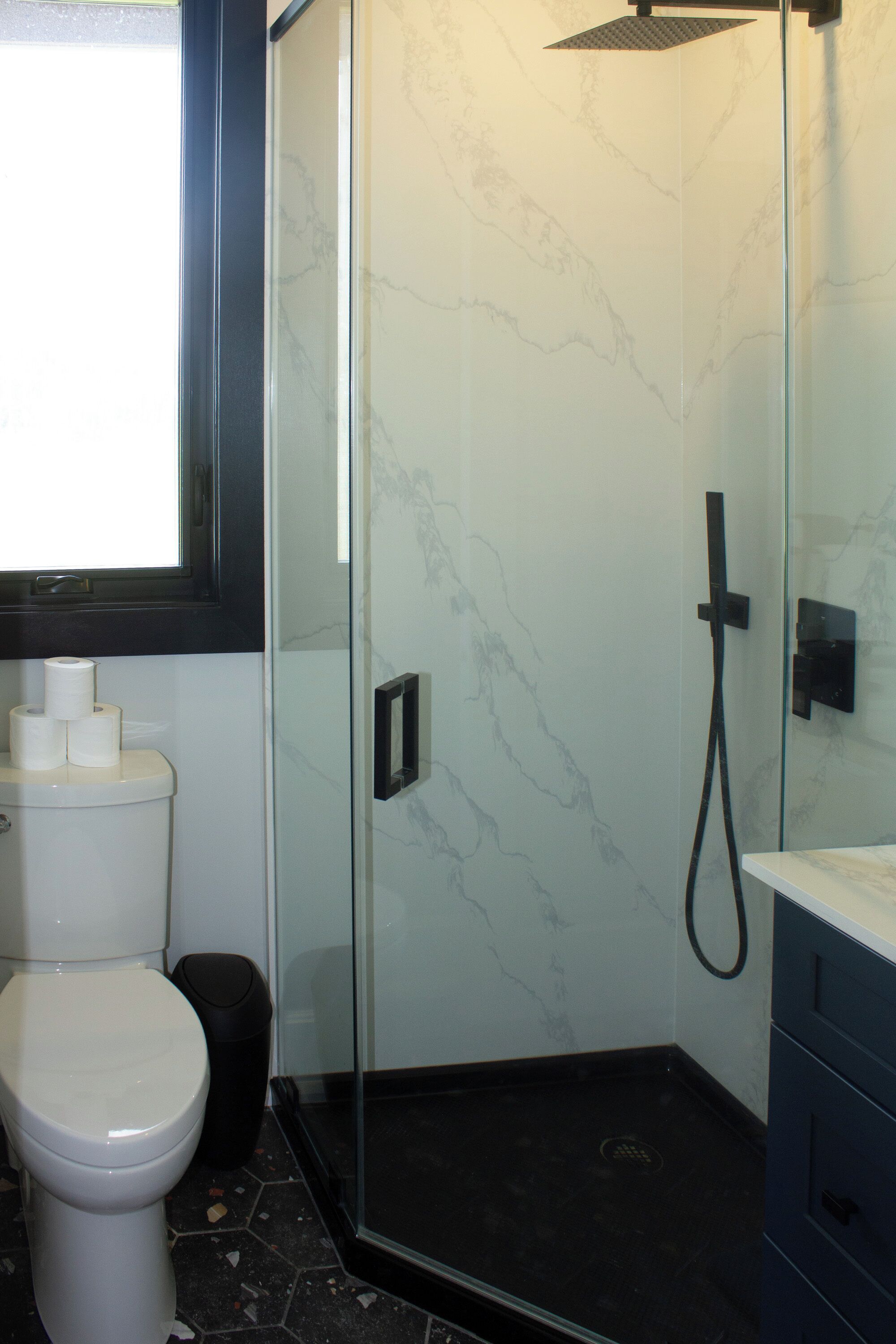 Baño con inodoro, cabina de ducha de vidrio y pared de mármol.