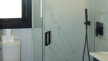 Baño con inodoro, cabina de ducha de vidrio y pared de mármol.