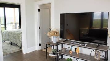A modern living room with a large flat-screen TV, a coffee table, and a bookshelf with decorative items.
