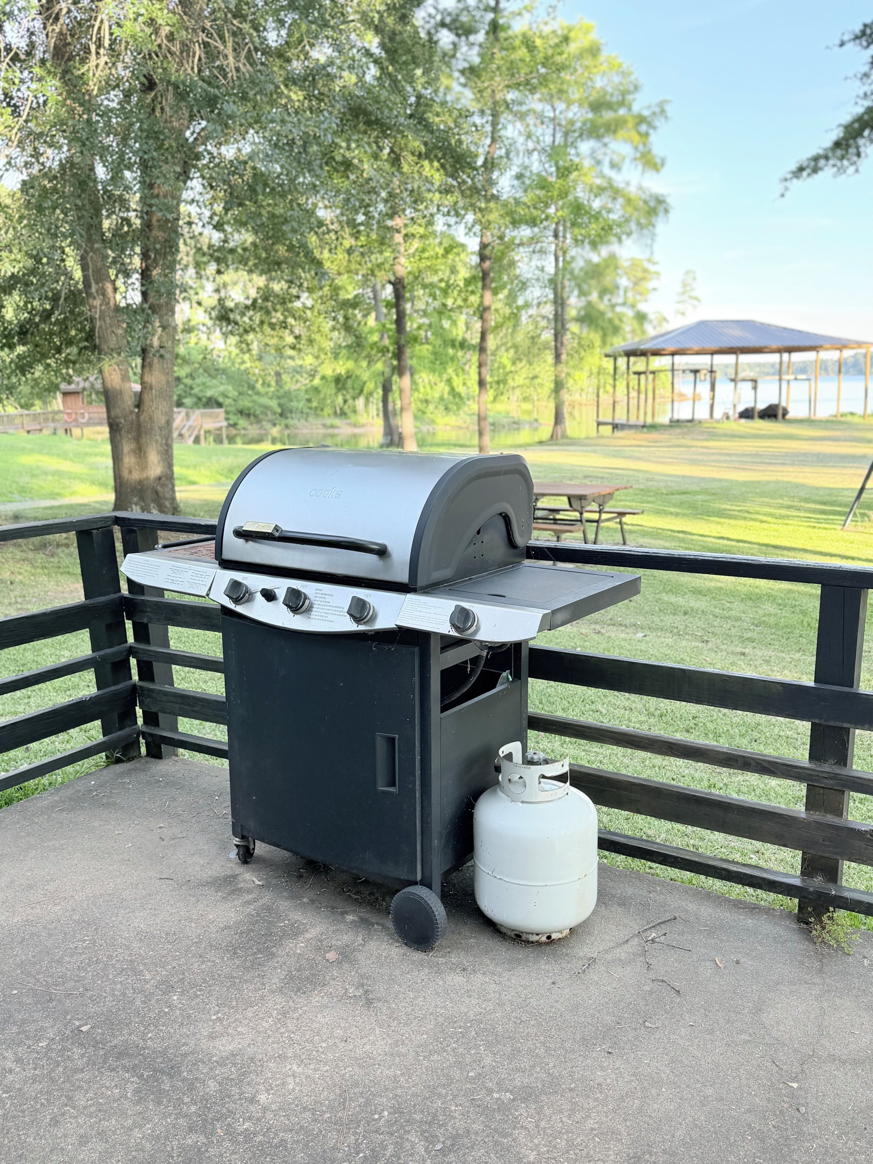 A portable grill with a gas tank, set on a concrete surface near a wooden fence.