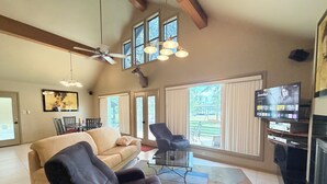 A spacious living room with a high ceiling, large windows, a ceiling fan, a fireplace, and a flat-screen TV mounted on the wall. - Pendleton Paradise Waterfront Cabin on Lanan Bay (Zwolle)