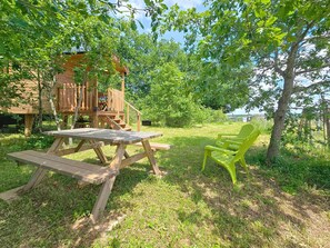 Un patio in legno con tavolo e sedie da picnic, immerso nel verde e alberi.