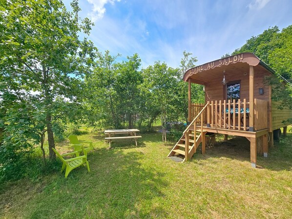 Una baita di legno con un cartello che riporta la scritta 'L'ANE AU SALON', un tavolo da picnic e una sedia verde.