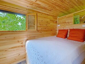 Una stanza in una baita di legno, con un letto, una finestra e un lampadario a parete.