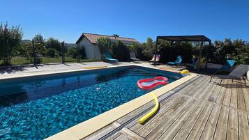 Piscina com deck de madeira, área de estar coberta e jardim cercado.