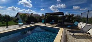 Una piscina rettangolare con un pontile in legno, circondata da lettini e un'area salotto coperta.