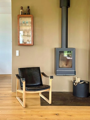 A room with a black leather chair, a wooden floor, a wall-mounted shelf with decorative items, a black fireplace, and a trash can. - Wake up to views of Kattegat and Samsø (Norsminde)