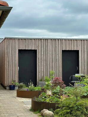 A modern building with two large doors, a brick pathway, and various potted plants. - Wake up to views of Kattegat and Samsø (Norsminde)