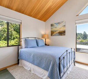 A bedroom with a bed, a window, a painting, and a lamp. - Love Nest | Ocean View Cottage & Hot Tub (Sea Ranch)