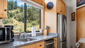 A kitchen with wooden cabinets, a stainless steel refrigerator, a microwave, and a sink. - Love Nest | Ocean View Cottage & Hot Tub (Sea Ranch)