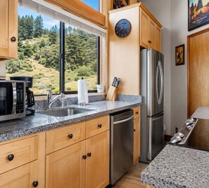 A kitchen with wooden cabinets, a stainless steel refrigerator, a microwave, and a sink. - Love Nest | Ocean View Cottage & Hot Tub (Sea Ranch)