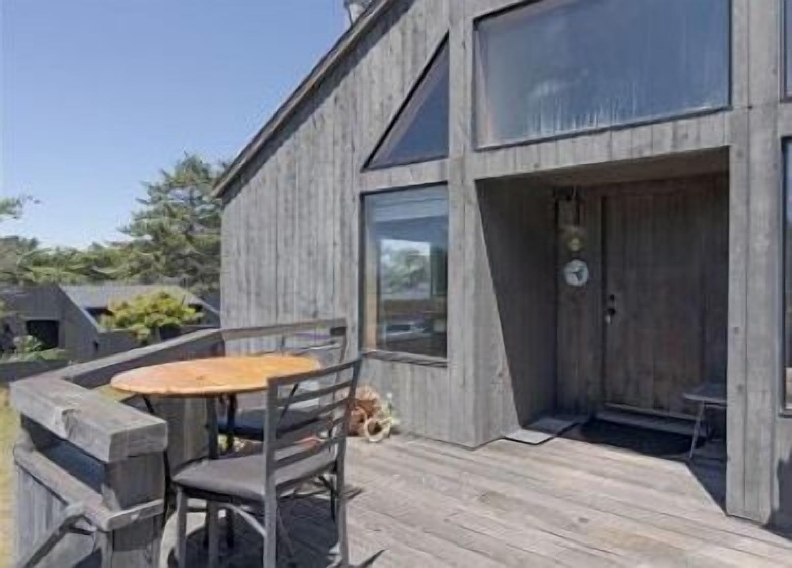 Eine Holzterrasse mit Tisch und Stühlen, ein großes Fenster und eine Tür.