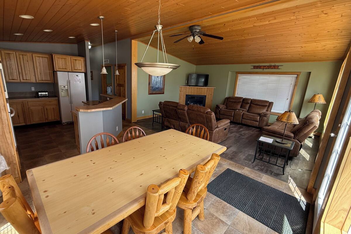 A spacious living area with a wooden dining table, brown leather sofas, and a ceiling fan.