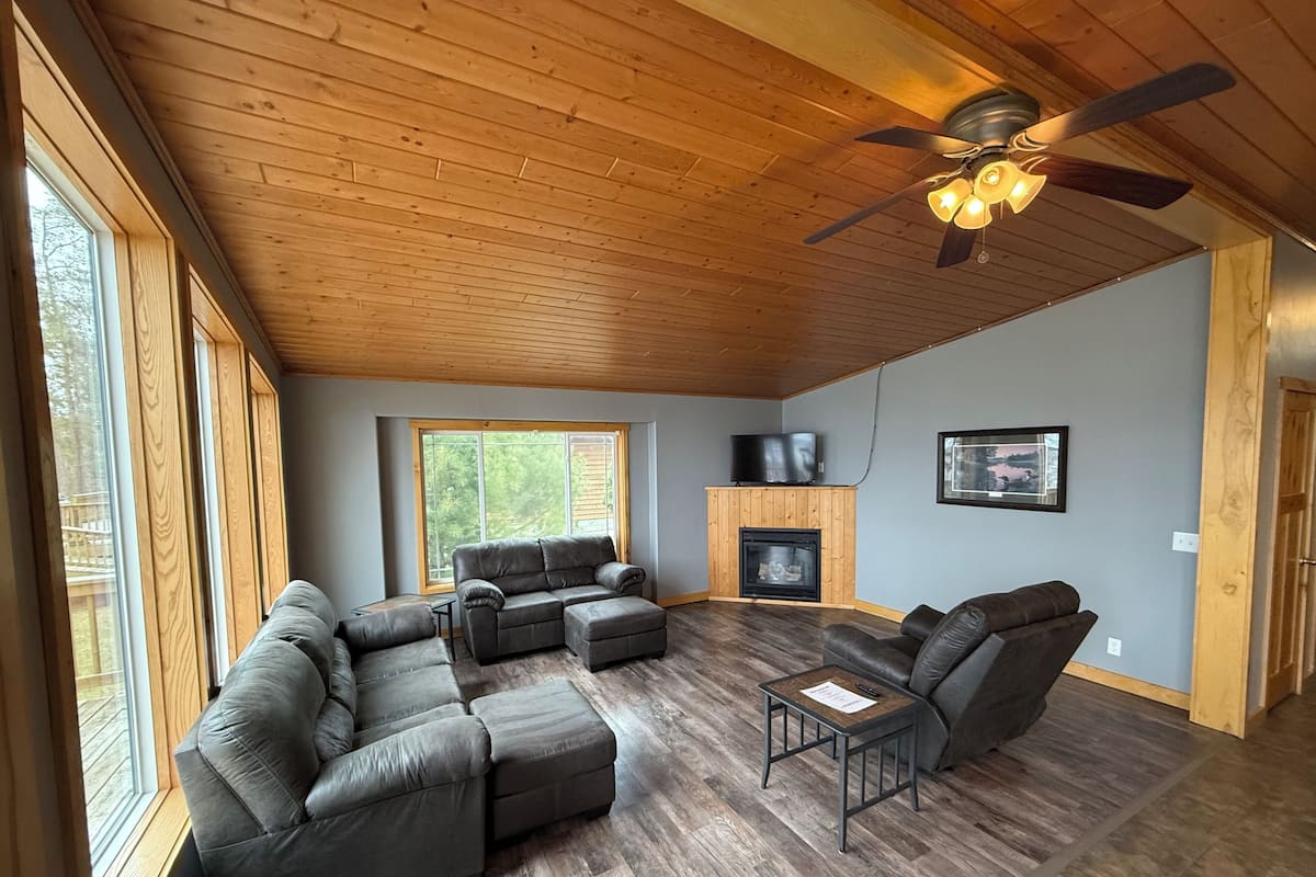 A living room with a sectional sofa, a fireplace, a ceiling fan, and large windows.