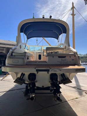 Un bateau doté d’un auvent bleu, de deux moteurs hors-bord et d’un espace salon avec une plateforme en bois.