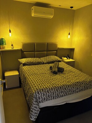 Ett hotellrum med en säng, sängbord, en luftkonditionering och en lampa.