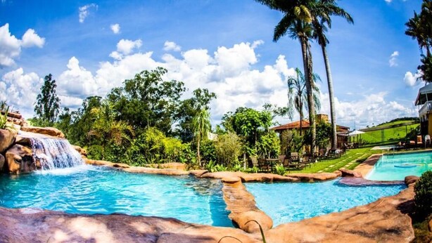 A pool area with a waterfall, palm trees, and a clear sky.