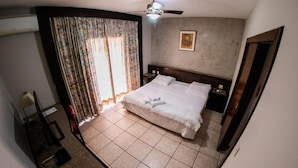 A bedroom with a bed, curtains, a ceiling fan, and a painting on the wall.