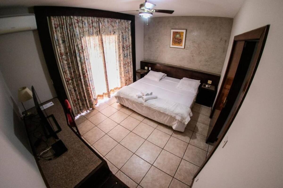 A bedroom with a bed, curtains, a ceiling fan, and a painting on the wall.