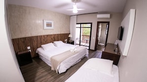A hotel room with two beds, a wooden headboard, a ceiling fan, a TV, and a balcony with a table and chairs.