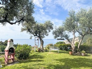 Un giardino con una panchina in pietra, una panchina in metallo e un cartello bianco.