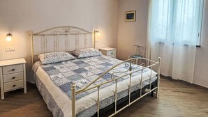 A bedroom with a bed, bedside tables, a nightstand, a chair, a window with curtains, and a wall-mounted picture. - Nice apartment in villa for 2 guests with WIFI, TV, balcony and pets allowed (Finale Ligure)