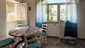 Un coin repas comprenant une table ronde en bois, deux chaises, un banc et une vue sur l’extérieur à travers une fenêtre ornée de rideaux.