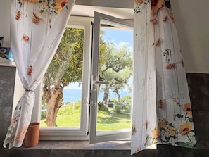 Una stanza con una porta-finestra scorrevole che si apre su un giardino con vista sul mare.