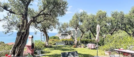 A garden with outdoor seating, a view of the sea, and a stone structure.