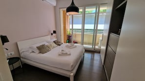 Ein Schlafzimmer mit Bett, Nachttischen, einer Lampe, einer Schiebeglastür zum Balkon und einem Fernseher.