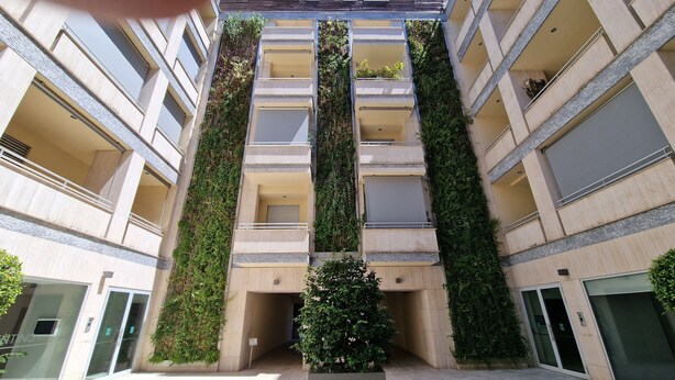 A multi-story building with vertical gardens on the exterior, a central entrance, and a small tree in the middle. - Domus Aventinae relax & fit (Roma)