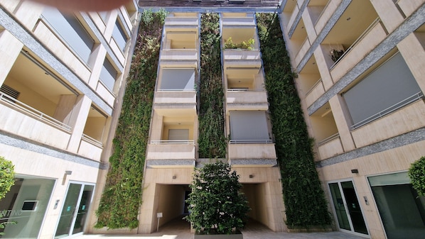 Ein mehrgeschossiges Gebäude mit vertikalen Gärten an der Außenfassade, einem zentralen Eingang und einem kleinen Baum in der Mitte.
